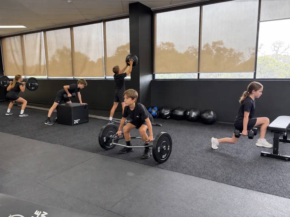 Kids doing strength training with barbells, dumbbells and medicine balls at The Huddle
